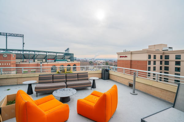 Rooftop terrace with orange and striped seating, metal railings, and city skyline view with stadium structure visible