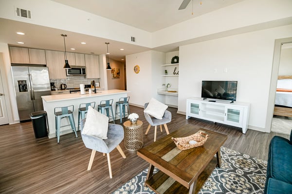 Open-plan living room and kitchen with island seating, wood table, gray chairs, TV, and stainless steel appliances