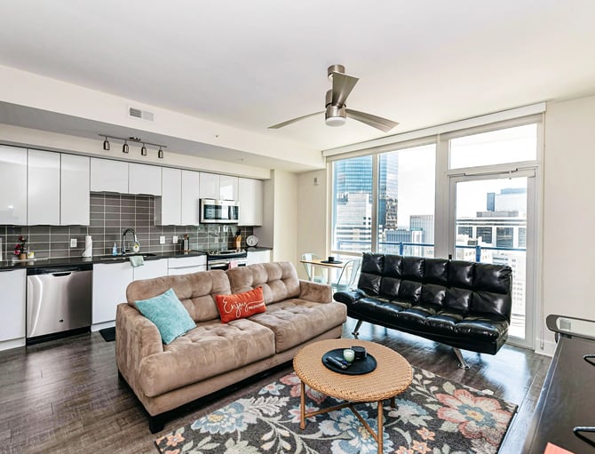 Open-plan living room and kitchen with city skyline view, beige and black sofas, round coffee table, and stainless steel appliances.